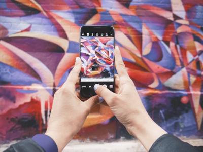 Hands holding a cellphone while photographing a colorful wall.